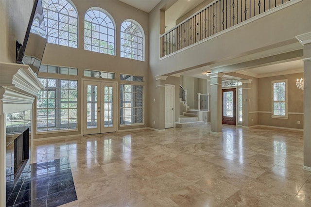 unfurnished living room with baseboards, stairs, french doors, ornamental molding, and decorative columns