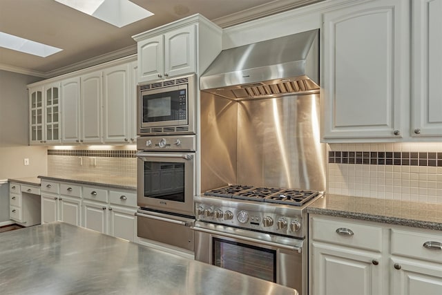 kitchen with stainless steel appliances, crown molding, wall chimney range hood, stainless steel counters, and a warming drawer