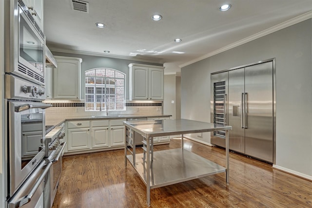 kitchen with dark wood-style flooring, visible vents, ornamental molding, a sink, and built in appliances