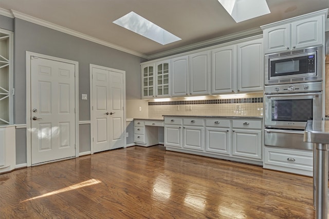 kitchen with a skylight, dark wood-style floors, appliances with stainless steel finishes, ornamental molding, and a warming drawer