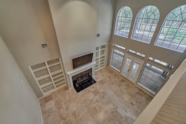 living room with built in features, french doors, visible vents, a towering ceiling, and a tiled fireplace