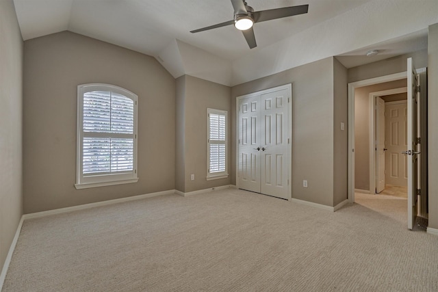 unfurnished bedroom with baseboards, a ceiling fan, light colored carpet, lofted ceiling, and a closet