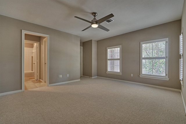 unfurnished bedroom with light carpet, baseboards, visible vents, a ceiling fan, and ensuite bath