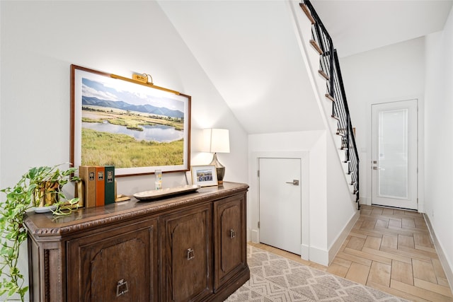 corridor with vaulted ceiling, a water view, stairs, and baseboards