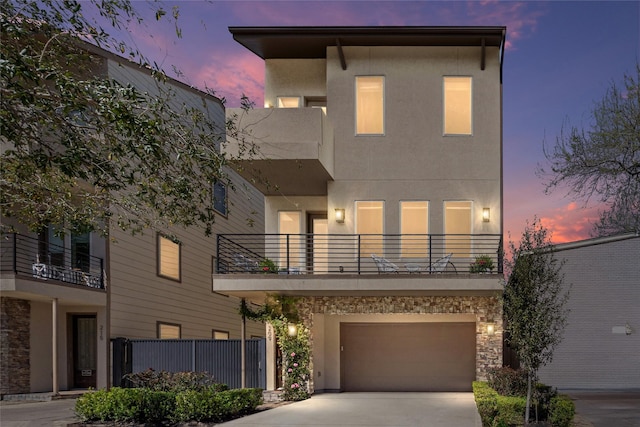 contemporary home featuring driveway, a garage, a balcony, stone siding, and stucco siding