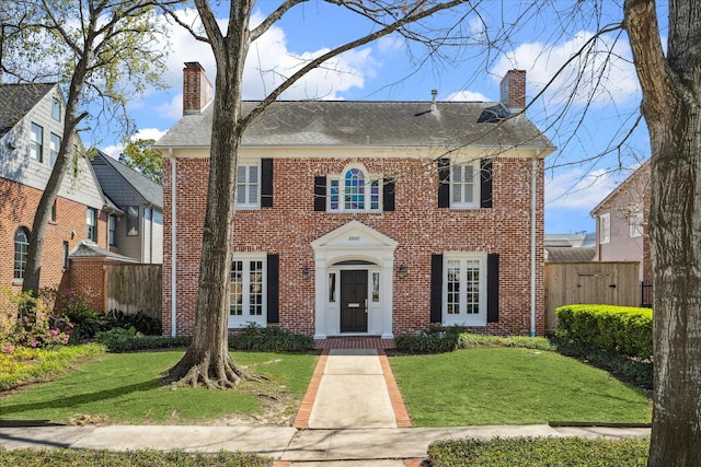 colonial inspired home featuring a front yard, brick siding, and a chimney