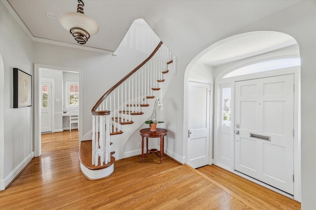 entrance foyer with crown molding, baseboards, stairs, light wood-style floors, and arched walkways