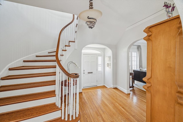 foyer entrance featuring light wood finished floors, stairway, arched walkways, and baseboards