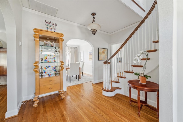 entrance foyer with visible vents, baseboards, ornamental molding, wood finished floors, and arched walkways