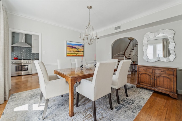 dining room with visible vents, stairway, light wood-style flooring, arched walkways, and a notable chandelier