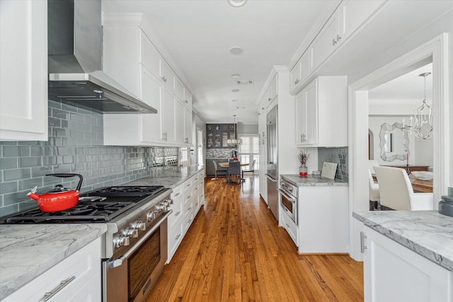 kitchen with premium appliances, white cabinets, light wood-type flooring, and wall chimney exhaust hood