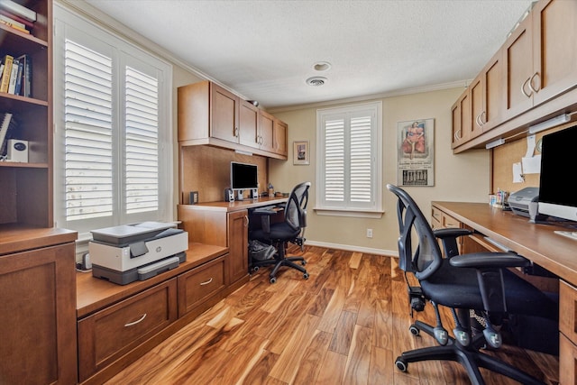 office space featuring built in study area, crown molding, baseboards, light wood-style flooring, and a textured ceiling