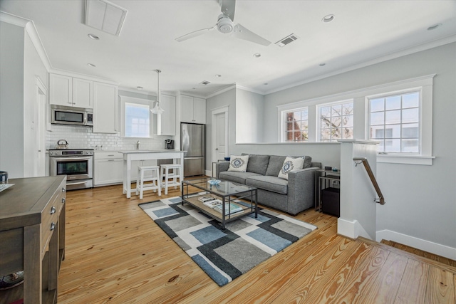 living area with light wood finished floors, visible vents, baseboards, ornamental molding, and recessed lighting