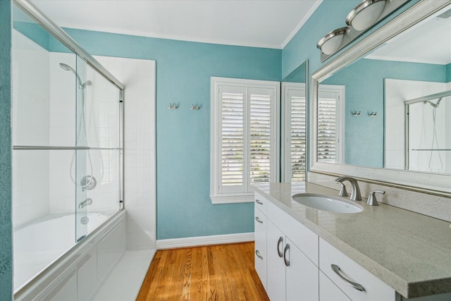 bathroom featuring wood finished floors, crown molding, baseboards, bath / shower combo with glass door, and vanity