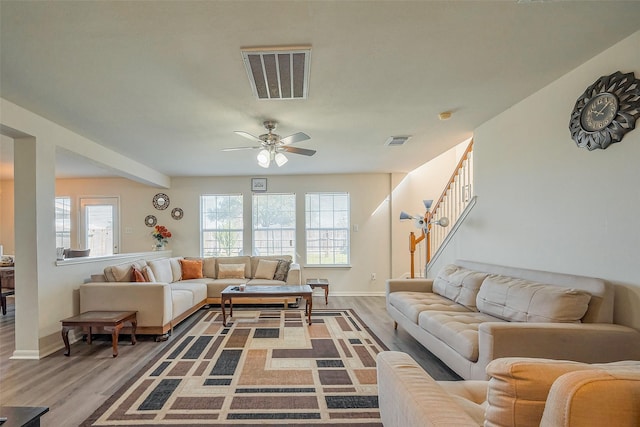 living room featuring light wood-style floors, stairway, visible vents, and a ceiling fan