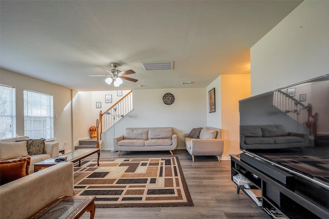 living area with baseboards, visible vents, ceiling fan, wood finished floors, and stairs