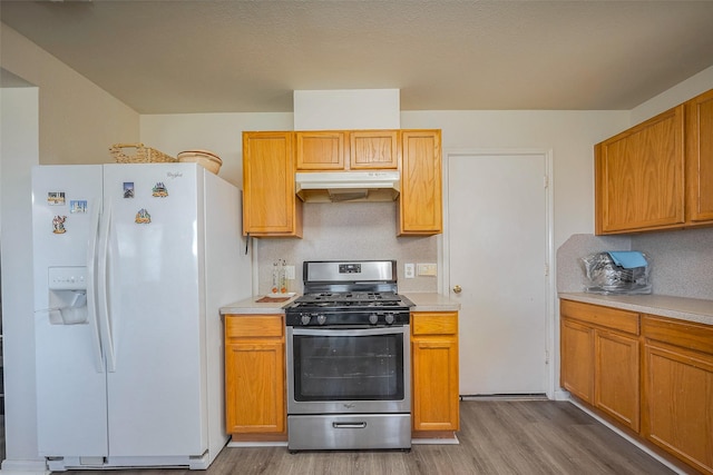 kitchen featuring light countertops, white refrigerator with ice dispenser, stainless steel range with gas stovetop, and under cabinet range hood