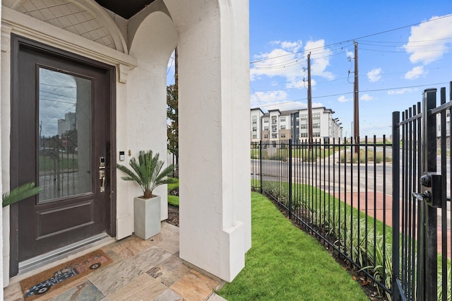 view of exterior entry with a yard, fence, and stucco siding