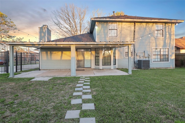 back of property at dusk featuring a patio, fence, a yard, cooling unit, and a chimney