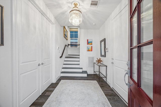 foyer entrance with stairs, dark wood-style flooring, visible vents, and an inviting chandelier