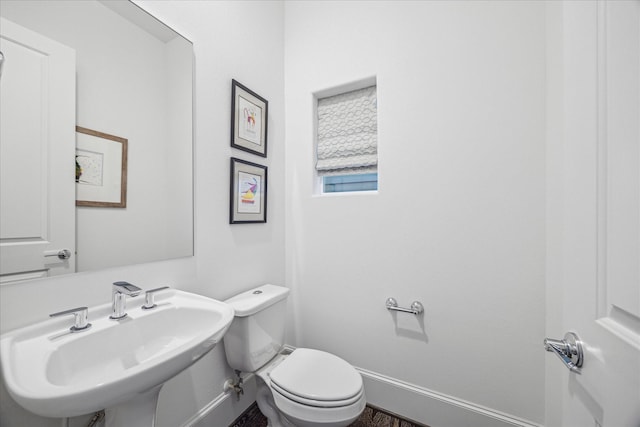 half bathroom with toilet, baseboards, and a sink