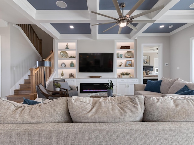 living area with coffered ceiling, a ceiling fan, stairway, beam ceiling, and a glass covered fireplace