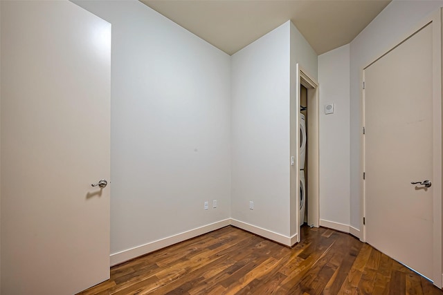 unfurnished bedroom featuring dark wood-style floors, baseboards, and stacked washer / drying machine