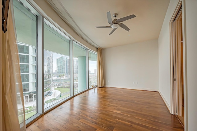 unfurnished room featuring baseboards, a ceiling fan, a city view, and wood finished floors