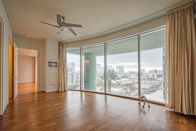 empty room with a ceiling fan, a city view, baseboards, and wood finished floors