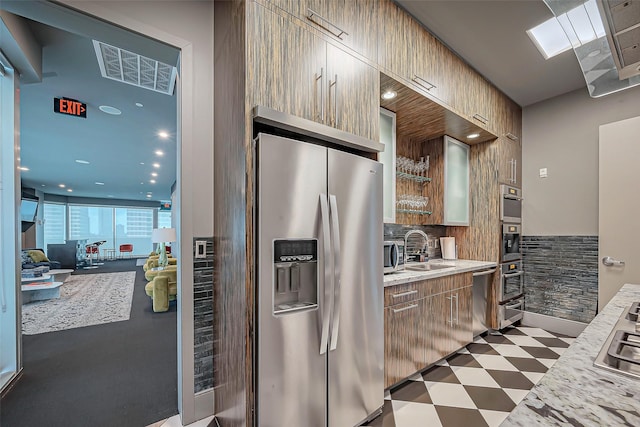 kitchen with dark floors, stainless steel appliances, a sink, light countertops, and decorative backsplash