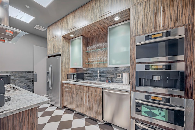 kitchen featuring light stone counters, light floors, tasteful backsplash, appliances with stainless steel finishes, and a sink