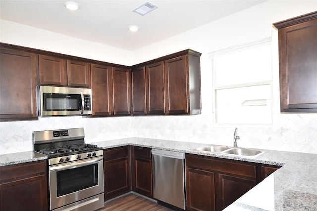 kitchen featuring dark brown cabinetry, visible vents, appliances with stainless steel finishes, light stone countertops, and a sink