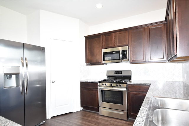 kitchen featuring stainless steel appliances, decorative backsplash, dark wood-type flooring, a sink, and light stone countertops