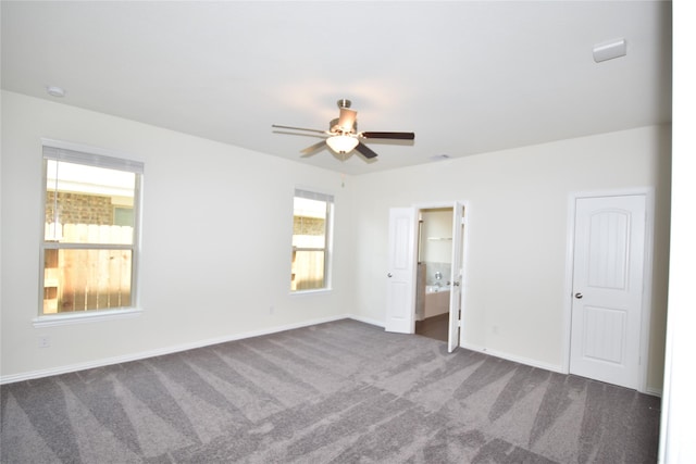 unfurnished bedroom with baseboards, dark carpet, ceiling fan, and connected bathroom