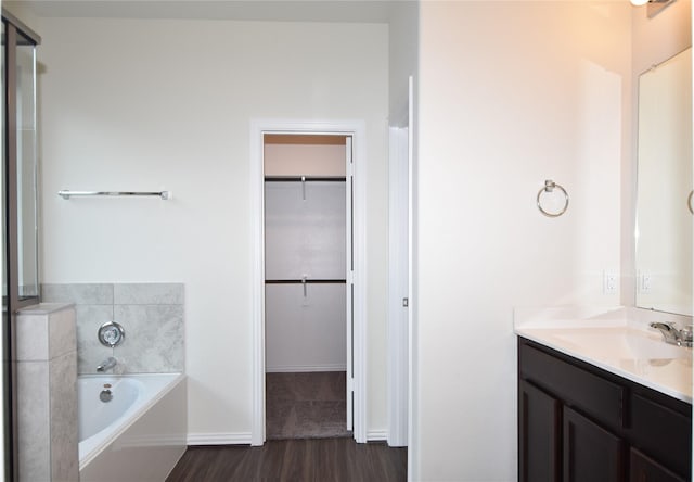 bathroom with a garden tub, a spacious closet, vanity, and wood finished floors