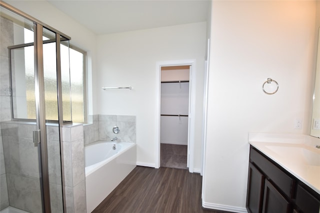 bathroom with a garden tub, wood finished floors, vanity, a shower stall, and a walk in closet