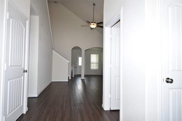 hall with high vaulted ceiling, arched walkways, dark wood finished floors, and baseboards