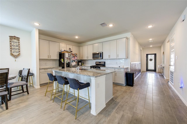 5723 Morning Vista Rd, Katy, TX 77493 - kitchen featuring light stone counters, a breakfast bar, a center island with sink, appliances with stainless steel finishes, and light wood-style floors