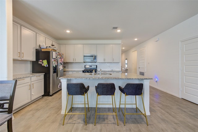 5723 Morning Vista Rd, Katy, TX 77493 - kitchen featuring a breakfast bar area, appliances with stainless steel finishes, a sink, light stone countertops, and light wood-type flooring