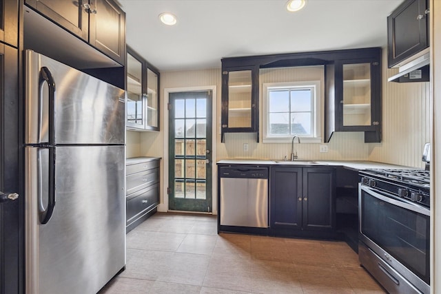 kitchen with stainless steel appliances, glass insert cabinets, a sink, and light countertops