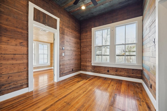 spare room featuring wooden walls, visible vents, baseboards, a ceiling fan, and hardwood / wood-style floors