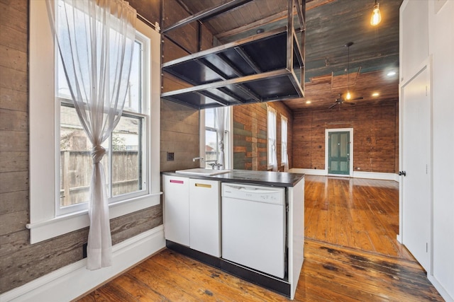 kitchen featuring dishwasher, wooden walls, a sink, and hardwood / wood-style flooring