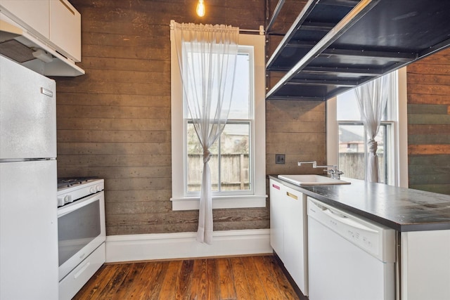 kitchen featuring white appliances, dark countertops, white cabinets, and wooden walls