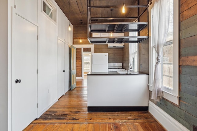 kitchen with dark countertops, white appliances, hardwood / wood-style floors, and wood walls