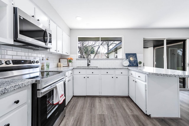 kitchen featuring stainless steel appliances, wood finished floors, a sink, white cabinets, and tasteful backsplash