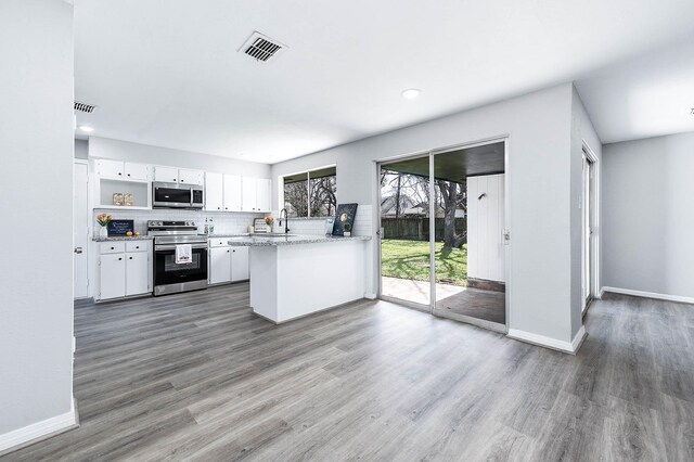 kitchen featuring visible vents, white cabinets, wood finished floors, a peninsula, and stainless steel appliances