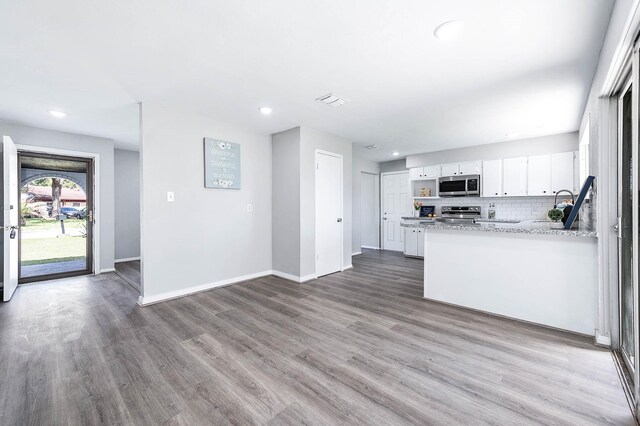 kitchen featuring backsplash, appliances with stainless steel finishes, white cabinets, wood finished floors, and baseboards