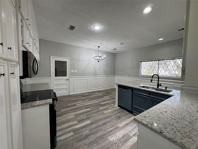 kitchen featuring a wainscoted wall, wood finished floors, a sink, white cabinets, and black appliances