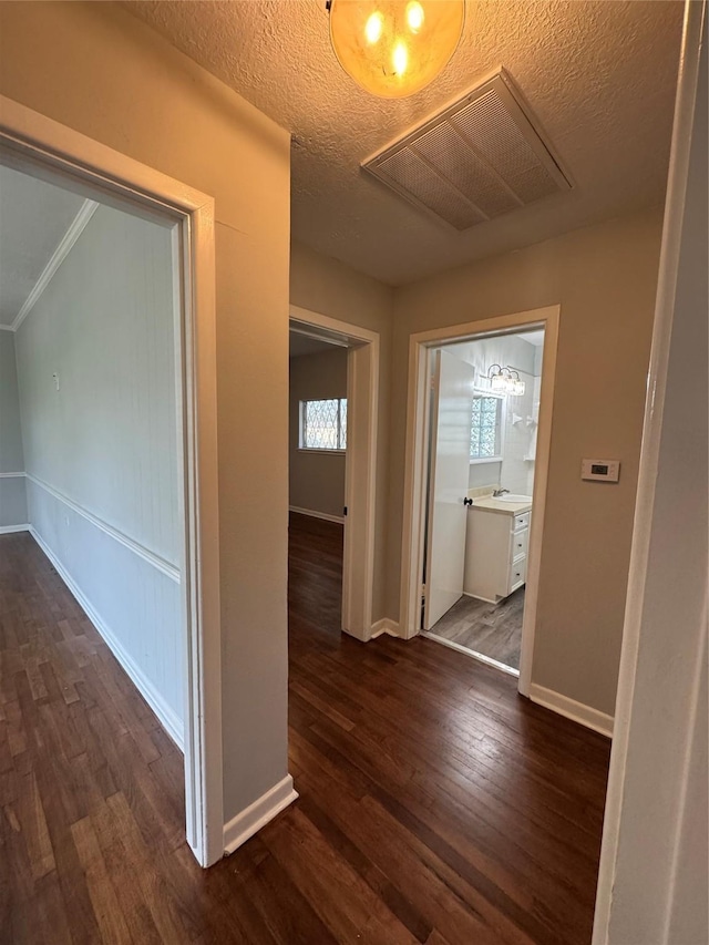 hall featuring dark wood-type flooring, visible vents, a textured ceiling, and baseboards