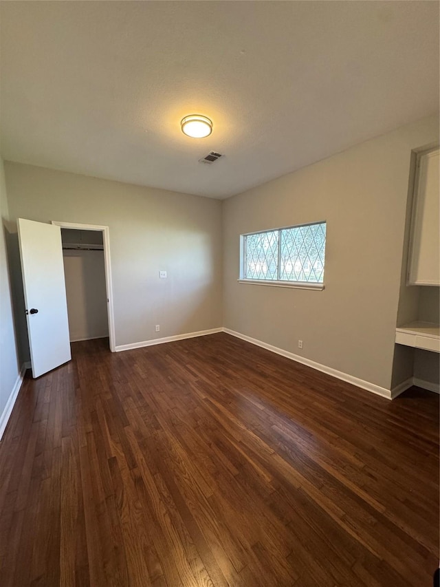 unfurnished bedroom with baseboards, visible vents, dark wood finished floors, and a closet